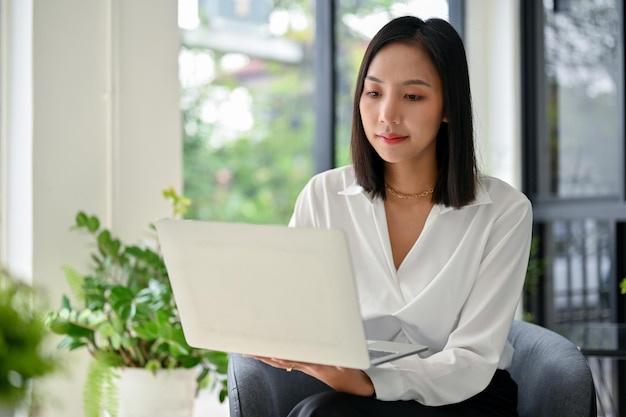 Atractiva mujer de negocios asiática que se centra en sus tareas comerciales en el trabajo remoto de una computadora portátil