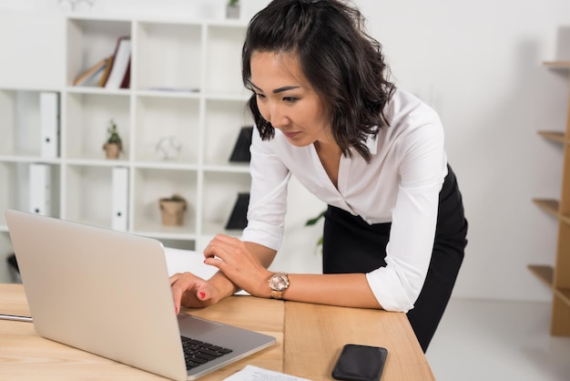 Atractiva mujer de negocios asiática que trabaja con una laptop en una oficina moderna