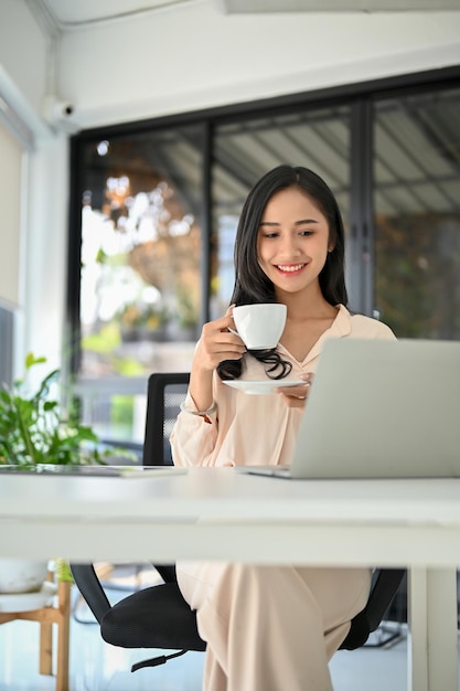 Atractiva mujer de negocios asiática tomando café mientras trabaja en sus tareas de negocios en la oficina