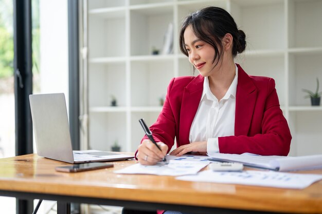 Una atractiva mujer de negocios asiática trabajando en sus tareas comerciales y mirando su portátil