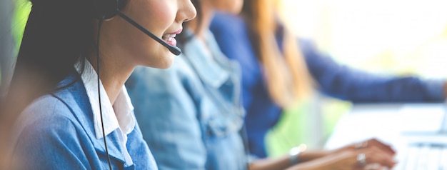 Atractiva mujer de negocios asiáticos en trajes y auriculares están sonriendo mientras trabajaba con la computadora en la oficina. Asistente de servicio al cliente trabajando en la oficina