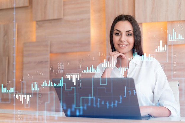 Foto atractiva mujer de negocios con camisa blanca en el lugar de trabajo que trabaja con una computadora portátil para optimizar la estrategia comercial en el fondo de finanzas corporativas holograma de gráfico forex sobre el fondo de la oficina