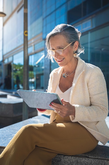 Atractiva mujer de negocios madura feliz trabajando con una tableta en una ciudad moderna