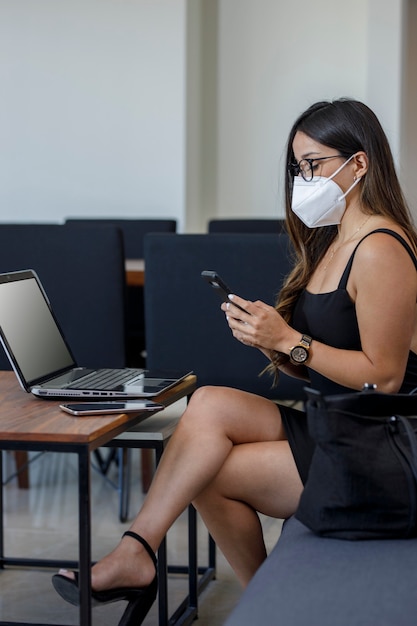 Atractiva mujer de negocios con máscara trabajando en su computadora desde casa enviando mensajes