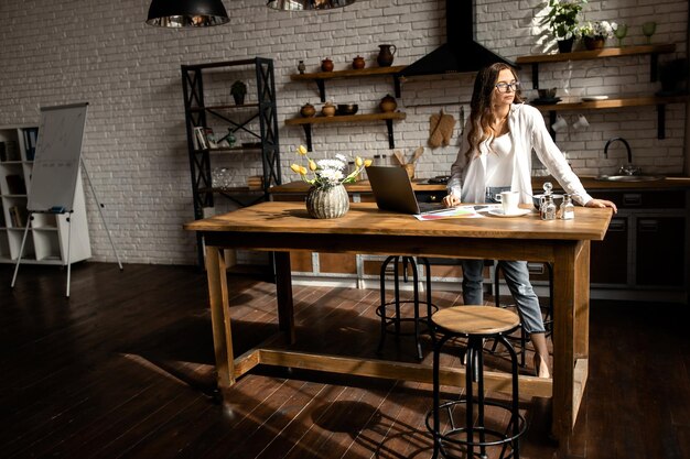 Atractiva mujer de negocios que trabaja con una computadora portátil en la cocina Concepto de trabajo desde casa