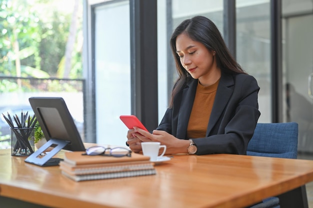 Atractiva mujer de negocios sentada en la oficina y usando teléfono móvil