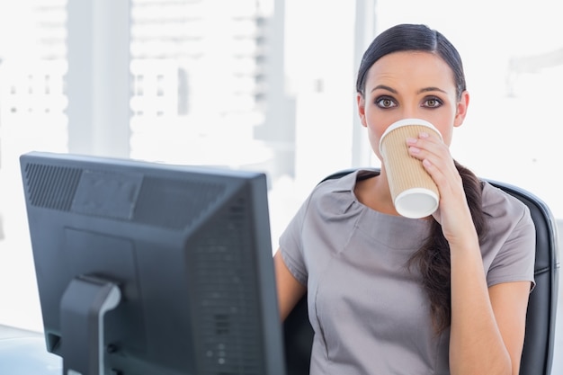 Atractiva mujer de negocios tomando café y mirando a cámara