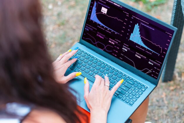 Una atractiva mujer de negocios trabaja en una computadora portátil mientras está sentada en una mesa en un café al aire libre en un cálido día de verano