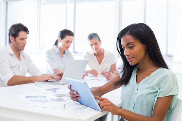 Atractiva mujer de negocios usando tableta con compañeros de trabajo detrás