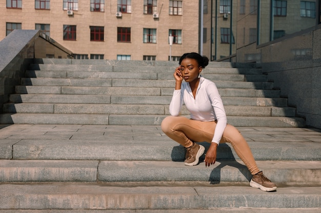 Atractiva mujer negra con estilo en las escaleras de la ciudad