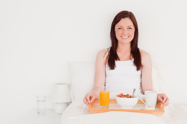 Atractiva mujer pelirroja desayunando mientras está sentado en su cama