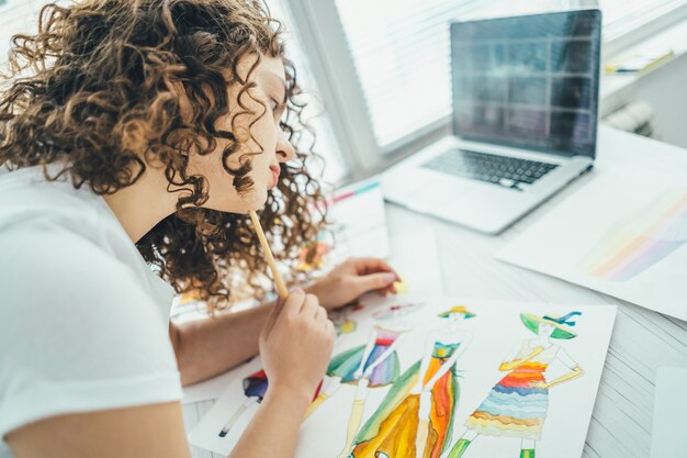 La atractiva mujer pintando un cuadro cerca de una computadora portátil