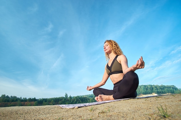 Atractiva mujer rizada pelirroja o modelo practicando yoga al aire libre