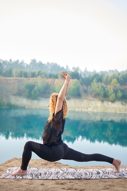 Atractiva mujer rizada pelirroja o modelo practicando yoga al aire libre