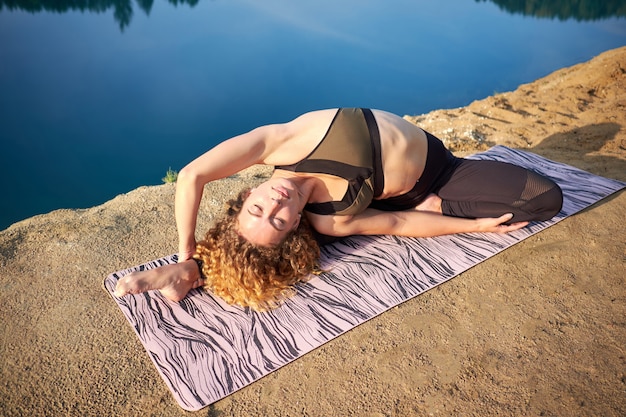 Atractiva mujer rizada pelirroja practicando yoga al aire libre