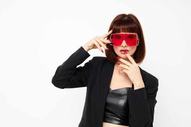 Atractiva mujer de rojo con elegantes gafas, un traje de cuero, chaqueta negra, fondo claro.