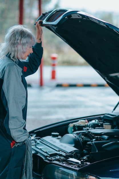 Atractiva mujer rubia joven vistiendo un uniforme mecánico de automóviles y reparando el automóvil