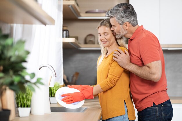 Atractiva mujer rubia madura lavando platos marido besándola