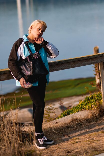 Foto atractiva mujer rubia de pie junto a una valla de madera con vistas a la costa