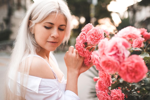 Atractiva mujer rubia sosteniendo flores rosas en el parque al aire libre