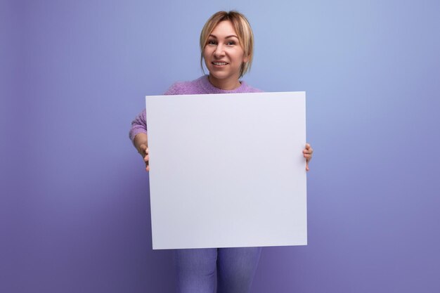 Atractiva mujer rubia sosteniendo una hoja de papel con una maqueta para un mensaje de promoción en un púrpura