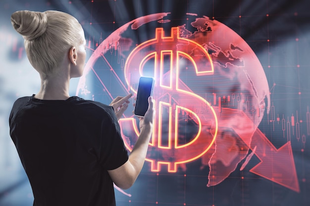 Atractiva mujer rubia usando un teléfono inteligente con holograma de flecha de dólar rojo global cayendo en el fondo interior de la oficina borrosa Recesión de caída del mercado y concepto de finanzas Doble exposición