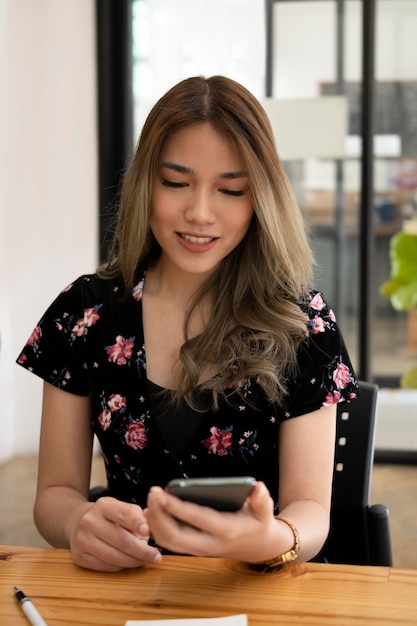 Atractiva mujer sentada en una cafetería y revisando las redes sociales en su teléfono inteligente