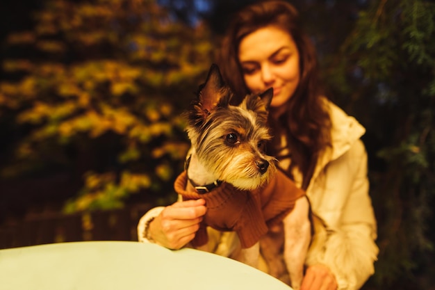 Atractiva mujer sentada con un perrito en la terraza de un café en la mesa centrada en el perro