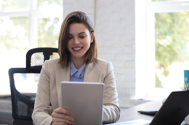 Atractiva mujer sonriente trabajando en una tableta en la oficina moderna.