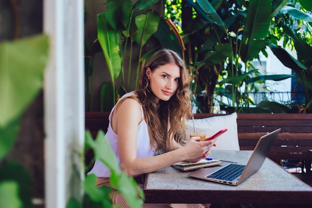 Atractiva mujer usando un teléfono inteligente en un café de verano