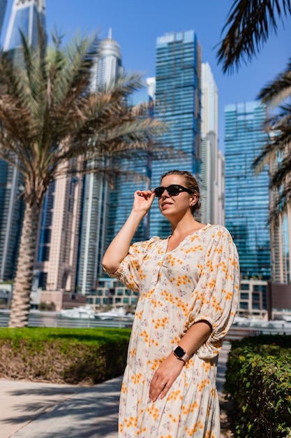 Atractiva mujer viajera con un vestido largo caminando por un paseo marítimo en el distrito de Dubai Marina Destinos de viaje y estilo de vida turístico en los Emiratos Árabes Unidos