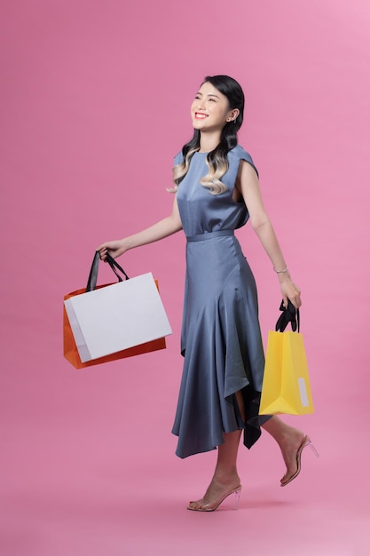 Atractiva mujer vietnamita sonriente con tacones altos y vestido azul caminando con bolsas de papel