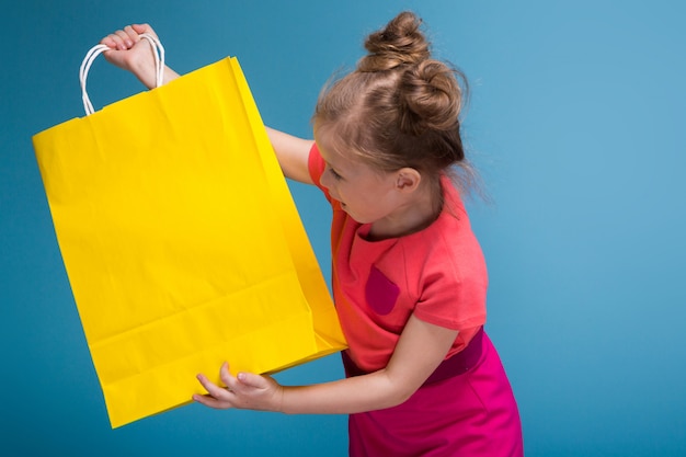 Atractiva niña linda en vestido rosa tiene bolsa de papel amarilla