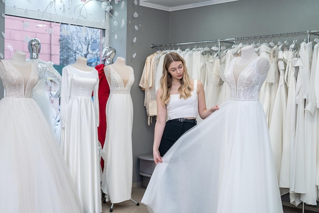 Atractiva novia eligiendo un vestido blanco en un moderno salón de bodas