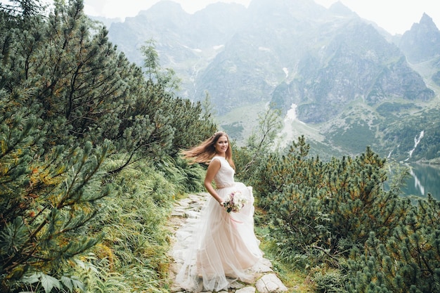 Atractiva novia morena con un hermoso vestido de novia blanco de pie cerca del lago Morskie Oko