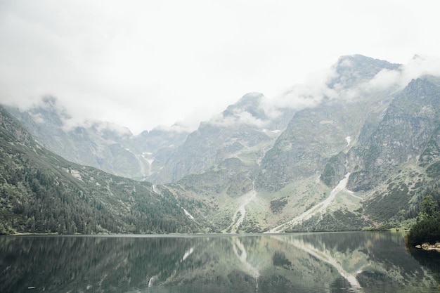 Atractiva novia morena con un hermoso vestido de novia blanco de pie cerca del lago Morskie Oko