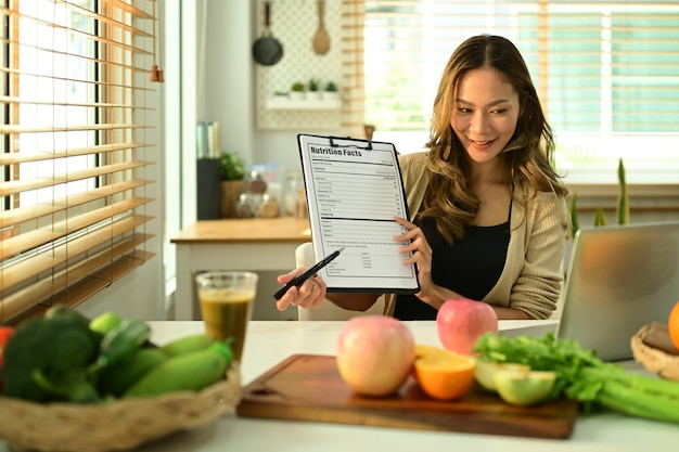 Atractiva nutricionista que muestra un ejemplo de menú semanal durante las consultas en línea a través de una computadora portátil Nutrición adecuada alimentación saludable