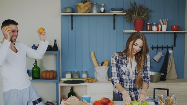 Foto atractiva pareja amorosa divirtiéndose en la cocina hombre guapo haciendo malabares con frutas