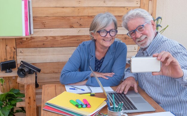 Foto atractiva pareja de ancianos sonriendo para un selfie sentado al aire libre con ordenador portátil