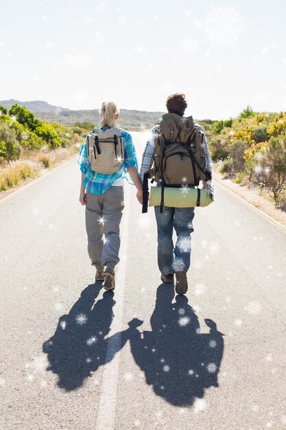 Atractiva pareja caminando por la carretera tomados de la mano contra la caída de nieve