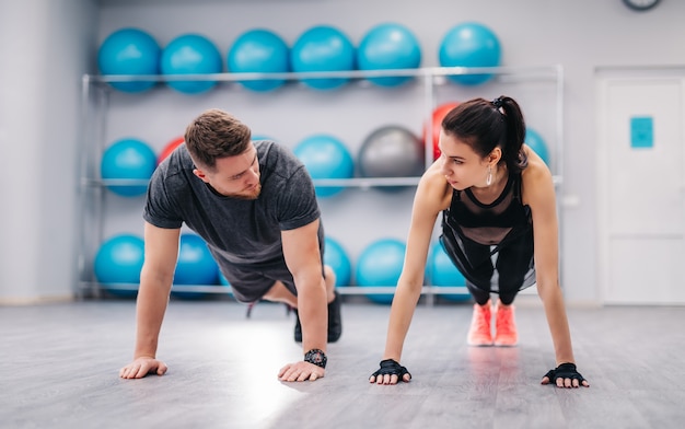 Atractiva pareja empujando el suelo y mirándose en el gimnasio.