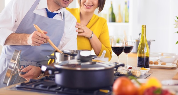 Atractiva pareja enamorada de cocinar y abre el vino en la cocina mientras preparan la cena para una velada romántica