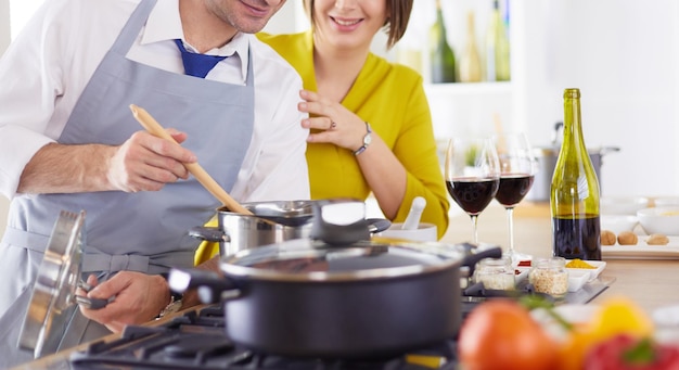 Atractiva pareja enamorada de cocinar y abre el vino en la cocina mientras preparan la cena para una velada romántica