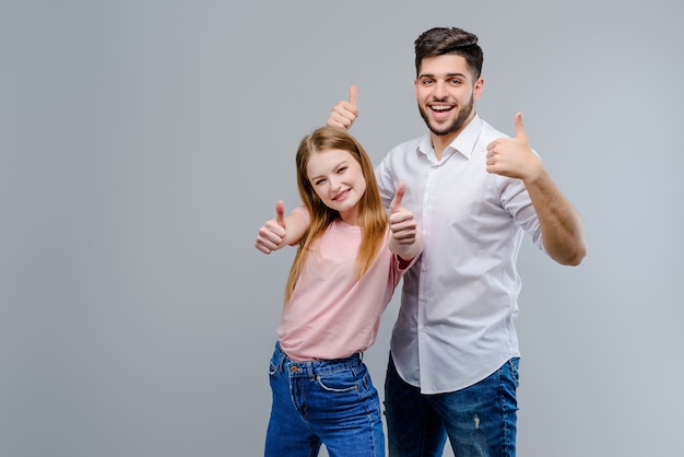 Atractiva pareja feliz muestra los pulgares arriba aislados sobre fondo gris