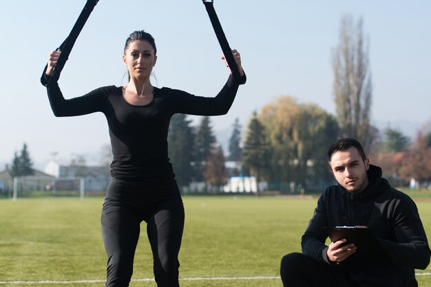 Atractiva pareja haciendo crossfit con correas de fitness Trx en el área del parque de la ciudad entrenando y haciendo ejercicio para el concepto de estilo de vida saludable de resistencia al aire libre