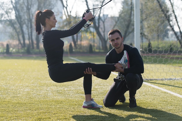 Atractiva pareja haciendo crossfit con correas de fitness Trx en el área del parque de la ciudad entrenando y haciendo ejercicio para el concepto de estilo de vida saludable de resistencia al aire libre