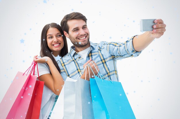 Atractiva pareja joven con bolsas de compras tomando un selfie contra la caída de nieve