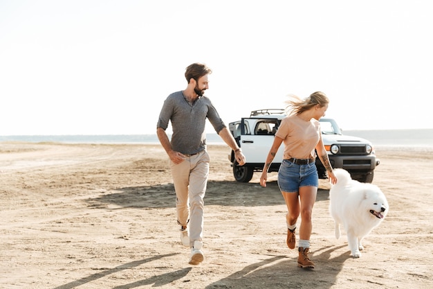 Atractiva pareja joven jugando con su perro en la playa soleada