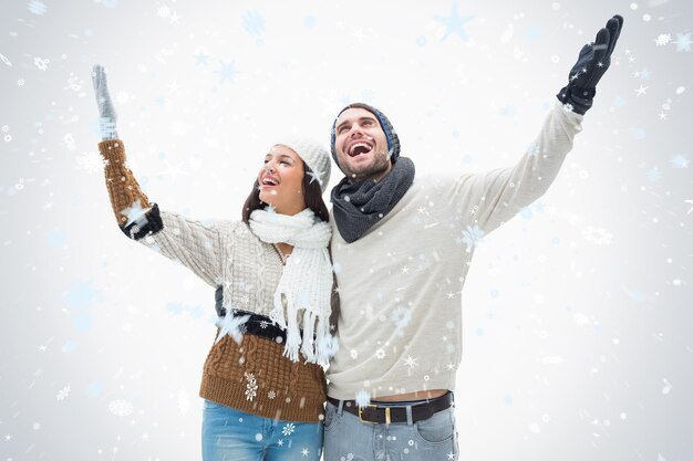 Atractiva pareja joven en ropa de abrigo con los brazos contra la nieve que cae