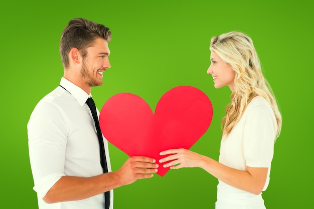 Atractiva pareja joven sosteniendo corazón rojo contra viñeta verde